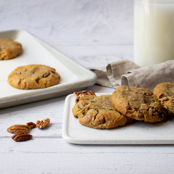 Candied pecan cookies placed on a ceramic plate, with a sheet tray and bottle of milk in the background.